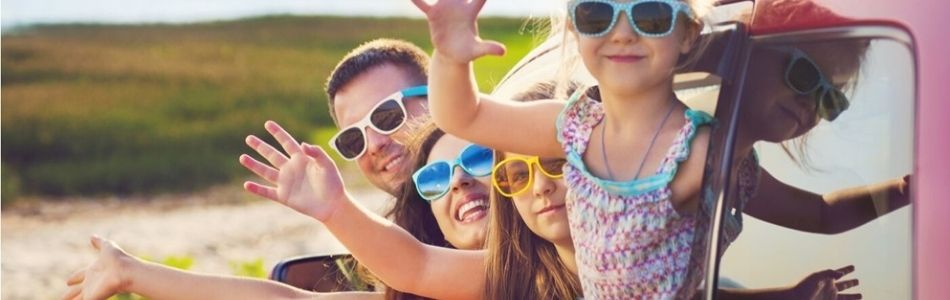 Een gezin in een auto met opgestoken handen, uitdrukking van blijdschap en enthousiasme tijdens hun reis.